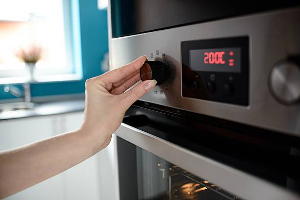 Close up of woman's hand setting temperature control on oven. The display shows the set temperature to 200 degrees Celsius